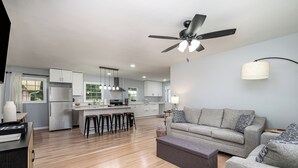 A modern kitchen with a central island, bar stools, and a ceiling fan.