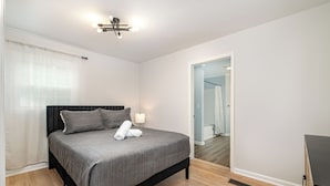 A bedroom with a bed, a bedside lamp, and a view of a bathroom through an open door.