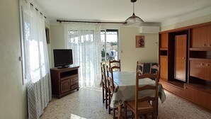 A living room with a TV, dining table, chairs, and a wooden cabinet. - Country house near the Ardèche (Saint-Paulet-de-Caisson)