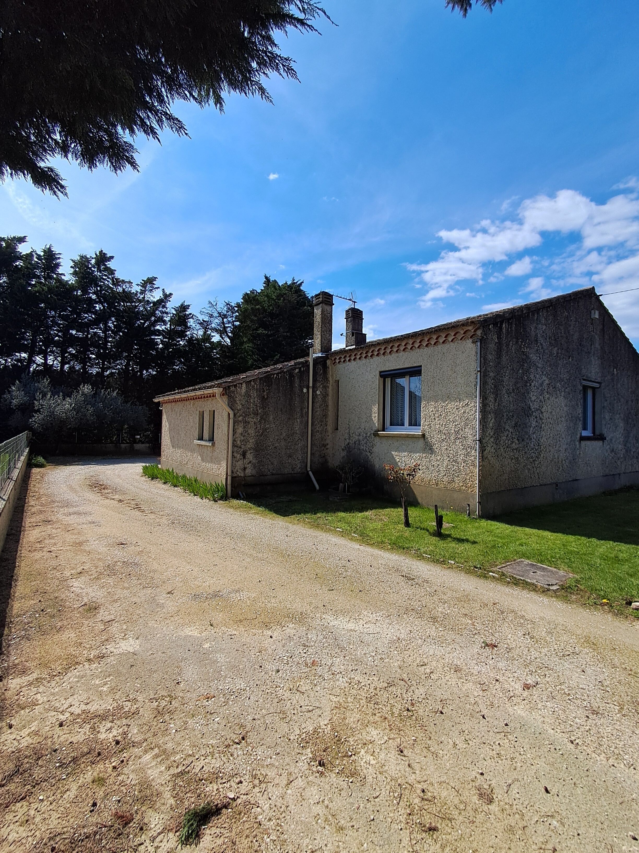 A rustic stone building with a gravel driveway, a small window, and a chimney.