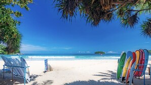 Une plage où des planches de surf sont alignées sur des supports, un ciel bleu dégagé et une mer calme.