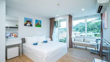 A modern hotel room with a large bed, a desk, and a balcony with a city view.