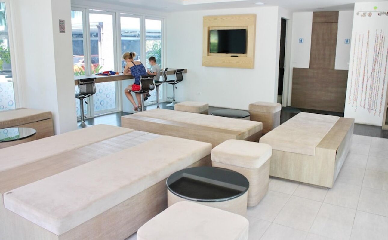 Un moderno salón de spa con camillas de masaje, un televisor y un amplio ventanal con vistas.