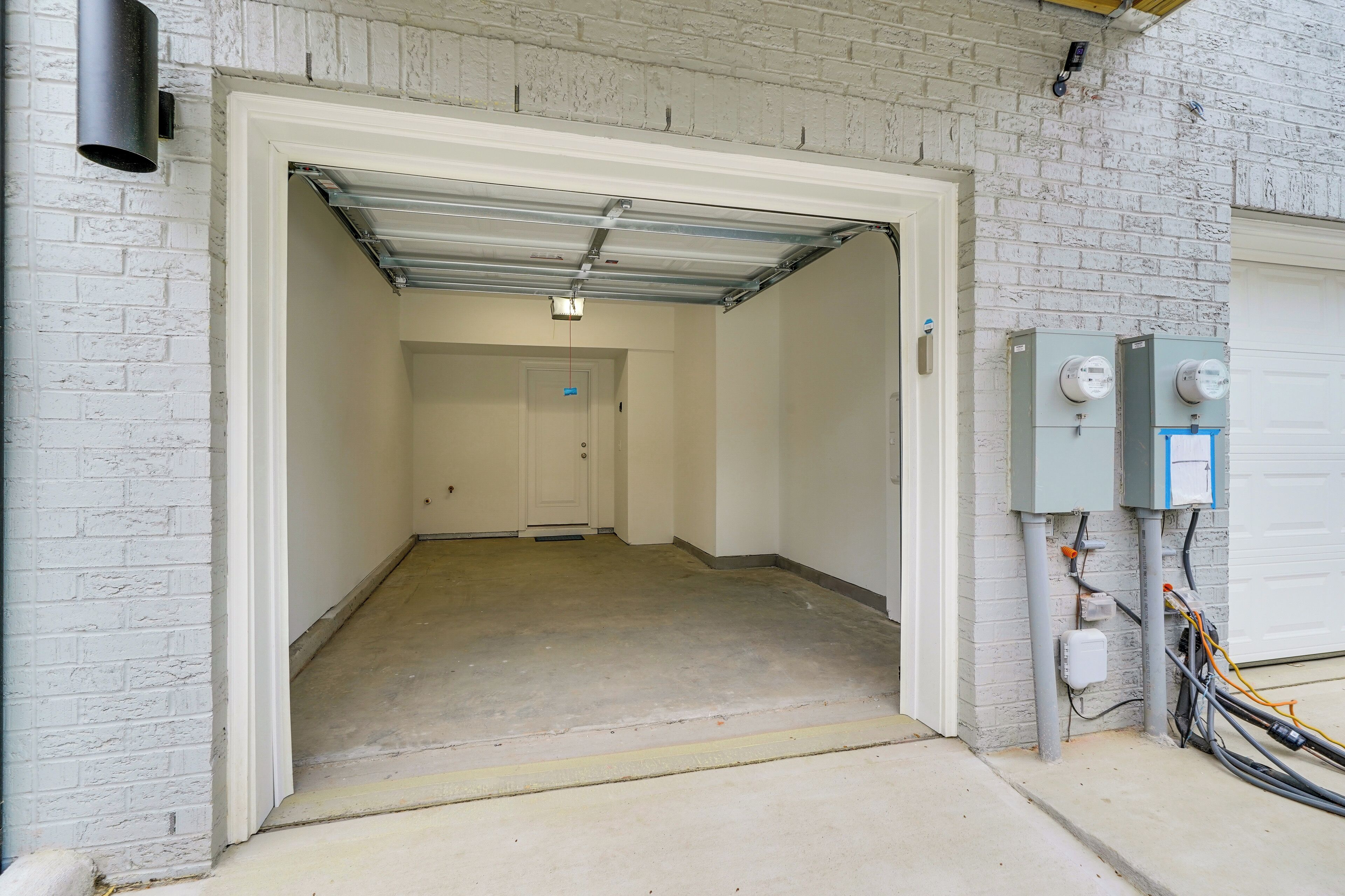 A garage entrance with a white door, a concrete floor, and electrical boxes on the right.