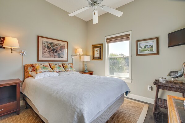 A bedroom with a large bed, a ceiling fan, a window with blinds, and wall-mounted lamps. - Marina & Golf Course Views: Edisto Island Home (Edisto Island)