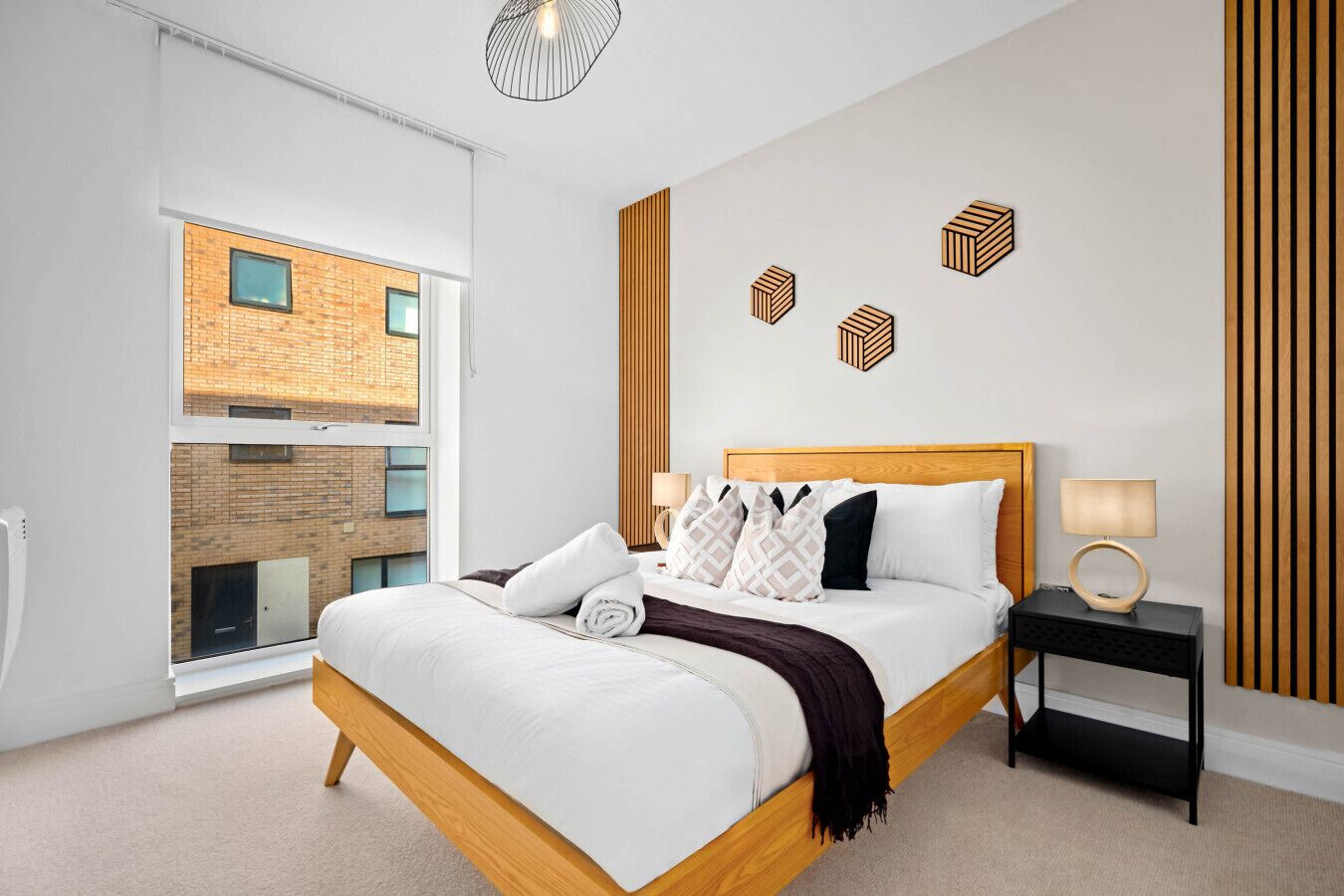 A modern bedroom with a large bed, a nightstand, a lamp, and a view of a brick building through a large window.