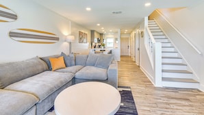 Ein modernes Wohnzimmer mit einem grauen Ecksofa, einem runden Couchtisch und einer Treppe, die zu einer zweiten Etage führt.