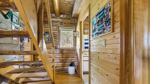 Interior de una cabaña de madera con una escalera, paredes de madera y una ventana.
