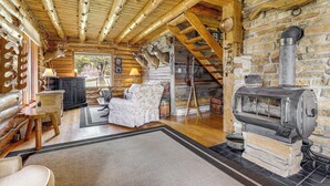 Interior de una cabaña de troncos con chimenea, muebles de madera y pared de piedra.