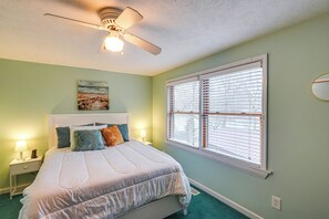 A bedroom with a bed, a ceiling fan, a window with blinds, a nightstand with a lamp, and a painting on the wall. - Lakefront Getaway w/ Fire Pit in Akron (Akron)