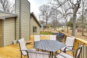 A deck with a table and chairs, surrounded by a wooden deck and trees. - Truman Lake Retreat: Relax and Unwind (Clinton)