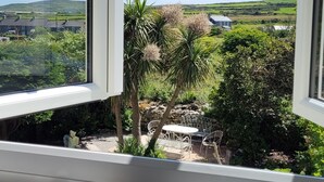 An open window with a view of a green landscape, a stone wall, and a white chair outside.