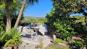 A patio with a table and chairs, surrounded by greenery and a stone wall.