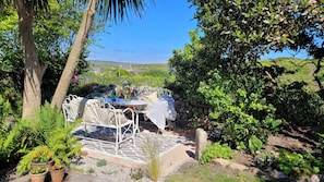A patio with a table and chairs, surrounded by greenery and a stone wall.