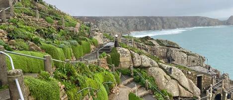 Un escalier qui descend vers la côte, offrant une vue sur la mer, et entouré de verdure et de constructions en pierre.