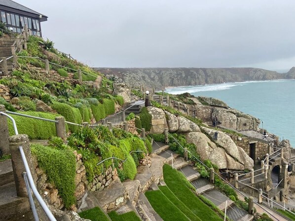 Una escalera costera con vistas al mar, rodeada de vegetación y construcciones de piedra.
