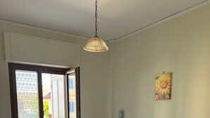Ein Schlafzimmer mit Bett, Nachttisch, Pendelleuchte, Glastür zum Balkon und einem Wandbild.