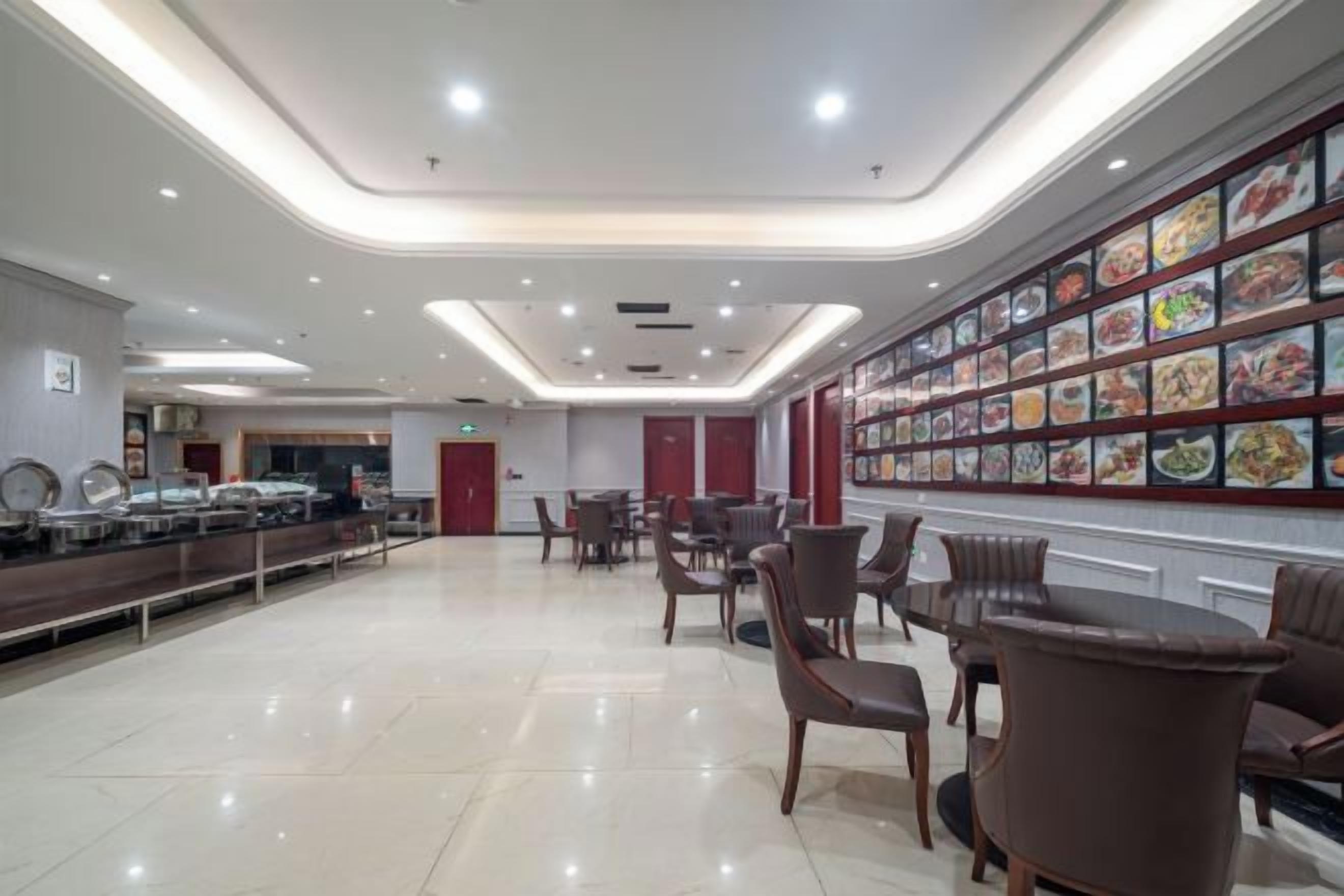 A spacious dining area with a buffet line, multiple dining tables, and a wall displaying various food images.