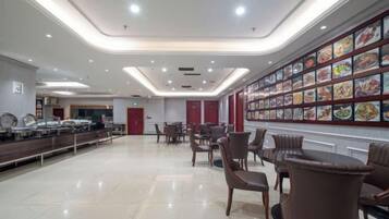 A spacious dining area with a buffet line, multiple dining tables, and a wall displaying various food images.