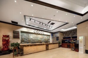 A hotel reception area with a marble counter, a decorative wall, and a ceiling with recessed lighting. - Yuzhou Peace Hotel (Hotan City)