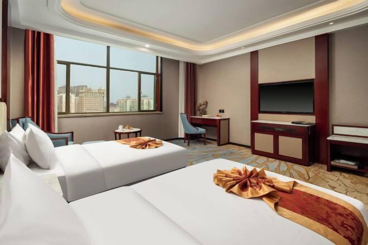 A hotel room with a large bed, a desk, a chair, a television, and a view of the city.