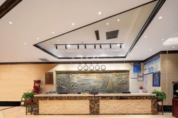 A reception desk with a marble top, surrounded by a low wall and a decorative mural. - Yuzhou Peace Hotel (Hotan City)