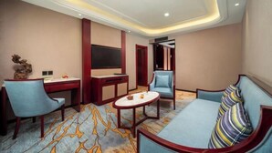 Una habitación de hotel con un sofá, dos sillones, un televisor, un escritorio y una alfombra estampada.