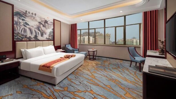 Habitación de hotel con una cama grande, un escritorio, una silla, una mesita y un ventanal con vistas a la ciudad.