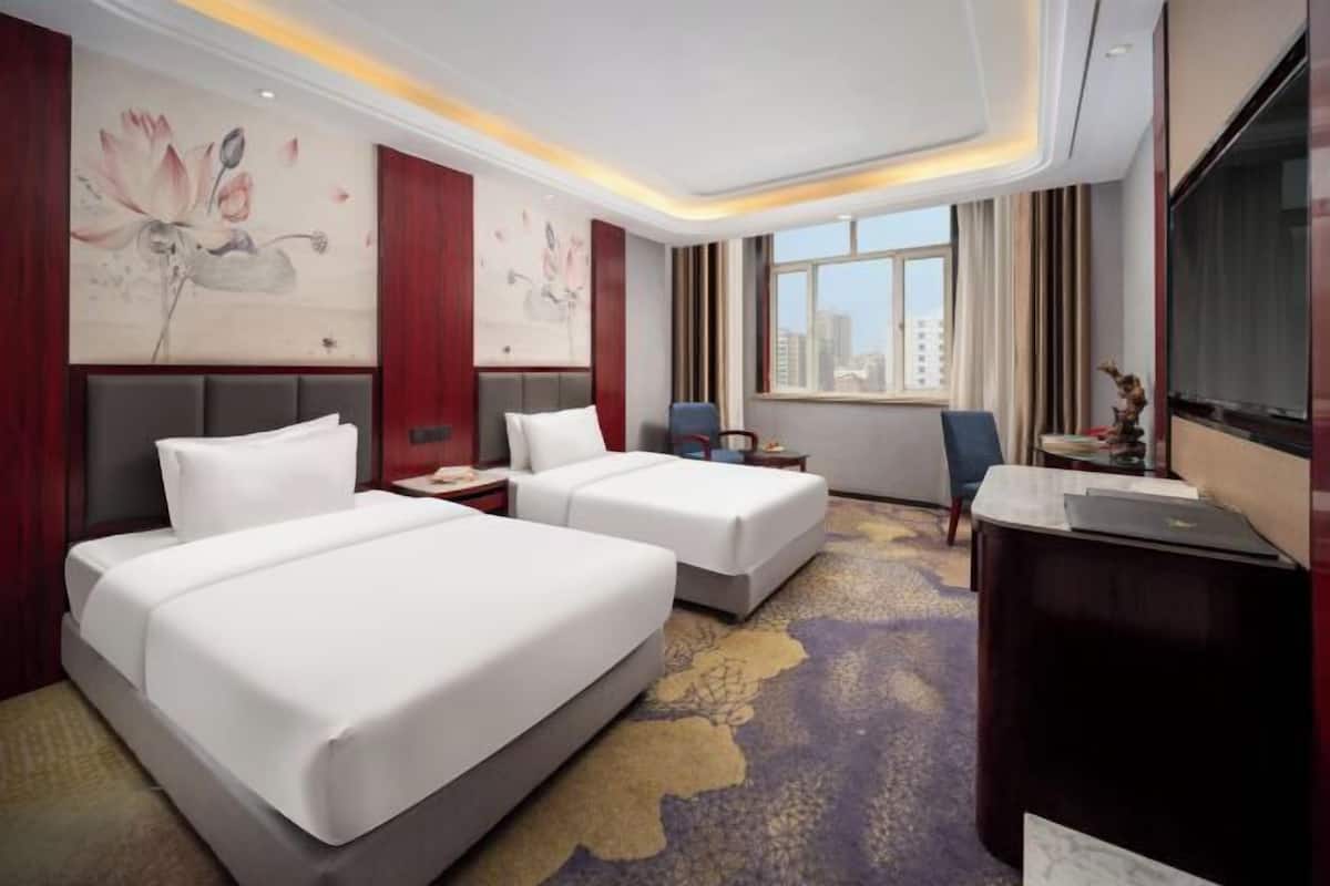 A hotel room with two beds, a desk, a chair, a TV, and a large window with a city view.