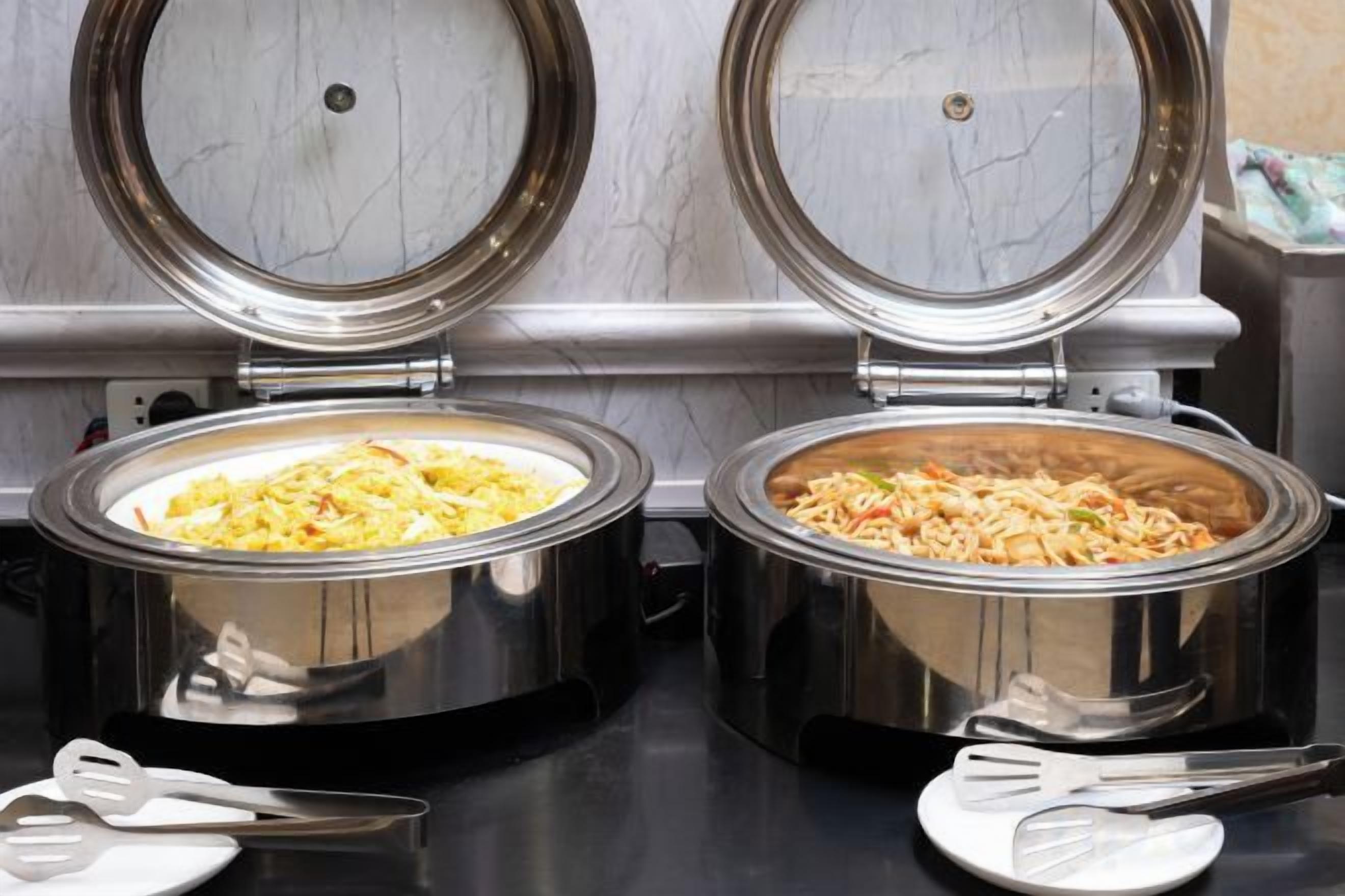 Two stainless steel food dispensers with lids open, containing what appears to be scrambled eggs and noodles.