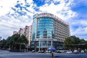 Un hôtel à plusieurs étages, doté d’une façade incurvée, de grandes fenêtres et d’une entrée imposante surmontée d’un auvent bleu.