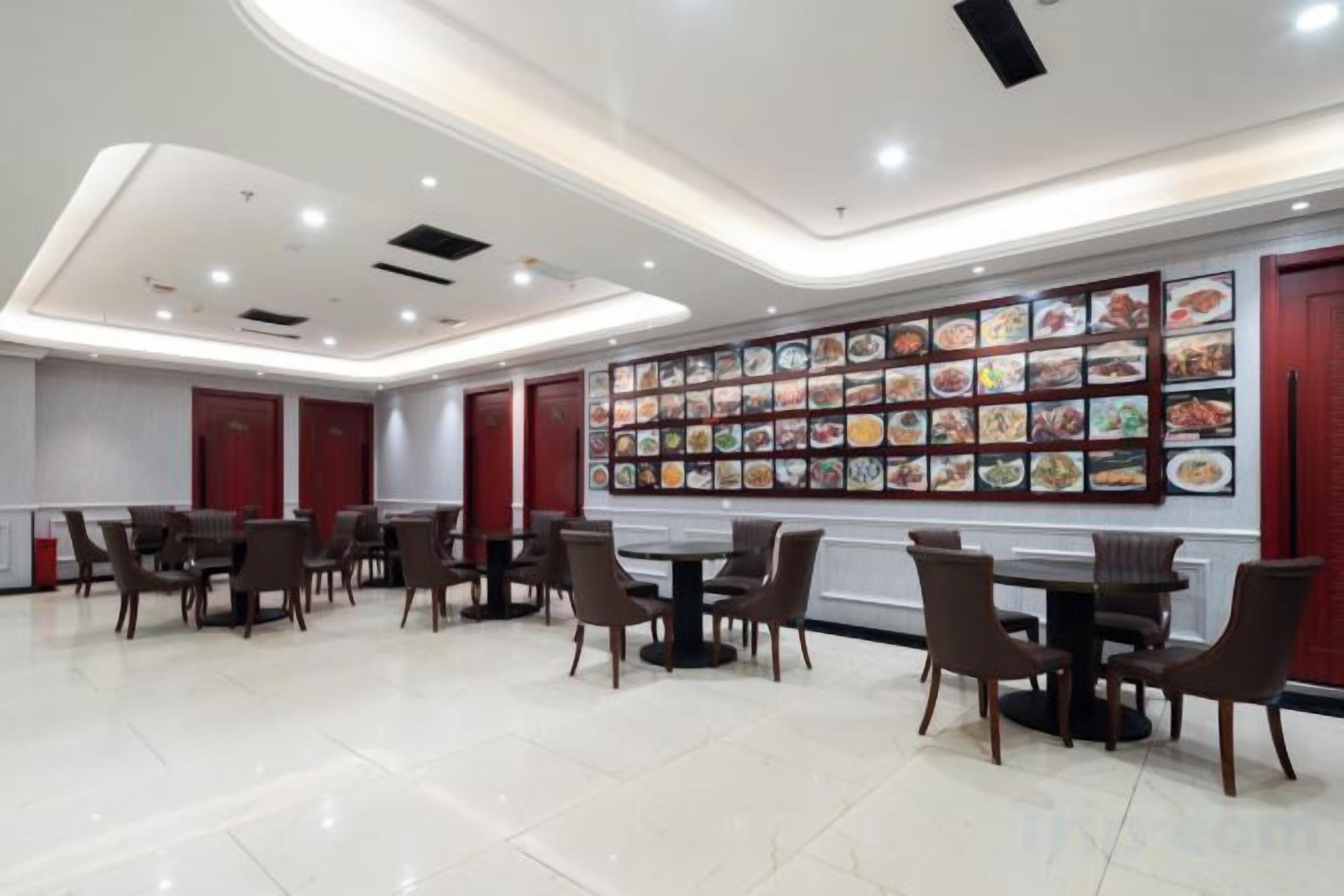 Un comedor con varias mesas y sillas, una pared con imágenes de comida y un diseño de techo moderno.