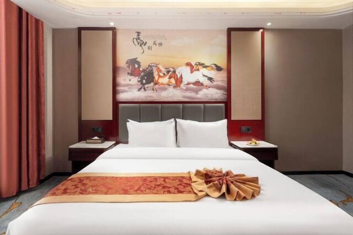 A hotel room with a large bed, a decorative wall painting, and a neatly arranged bedside table.