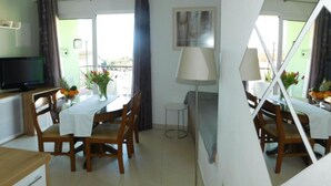A dining area with a table set for two, a television, and a window with curtains. - Apartments Roščić (Podgora)