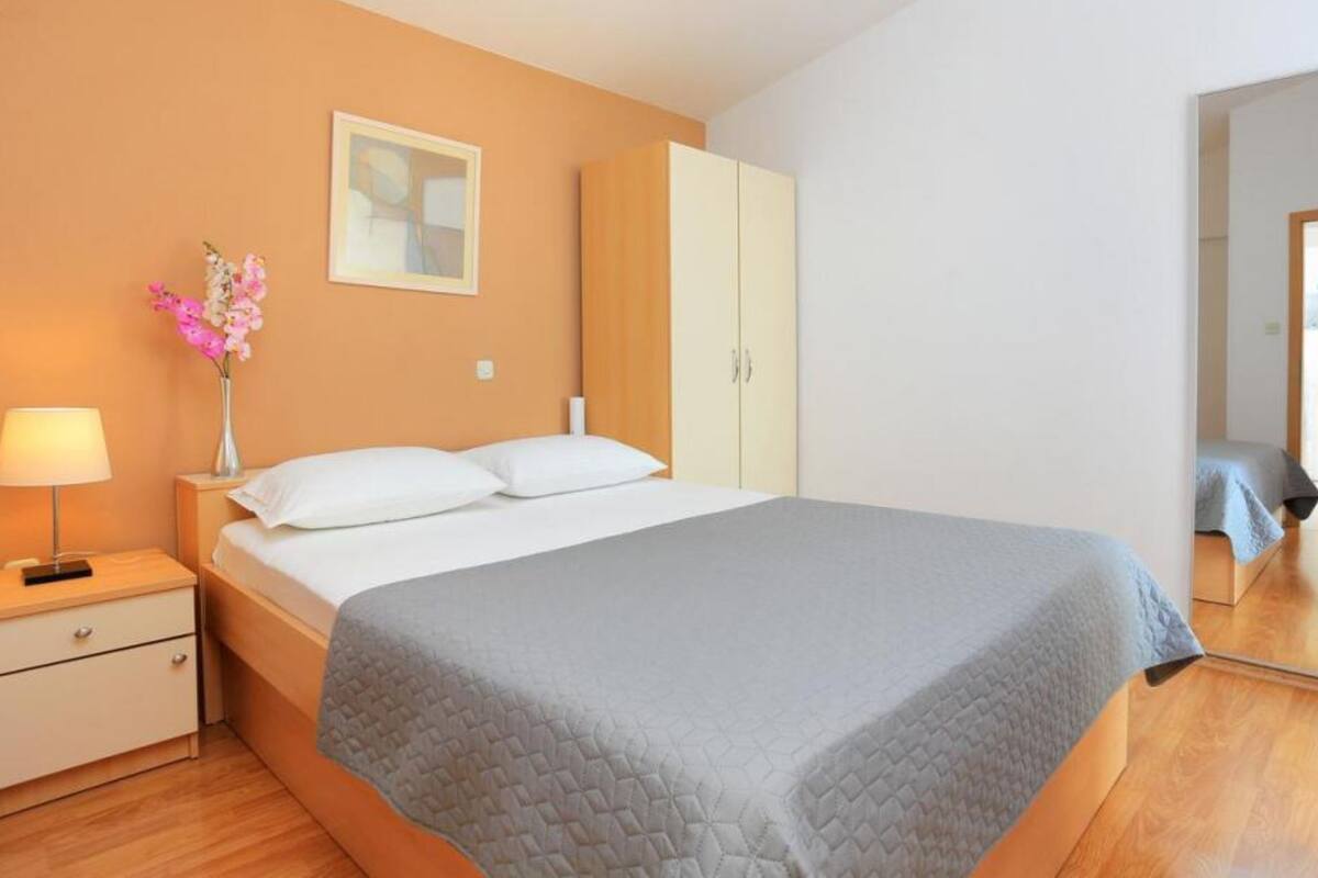 Une chambre à coucher avec un lit, une table de chevet, une lampe, un vase de fleurs et une armoire.