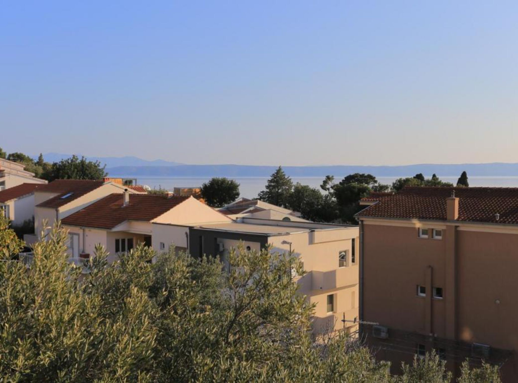 A residential area with modern houses, a clear view of the sea, and distant mountains.