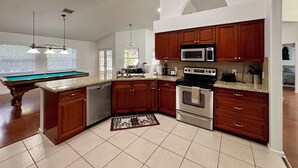 A kitchen with wooden cabinets, a microwave, an oven, a dishwasher, and a pool table. - Heated pool, pool table, heart of Wellington! (Wellington)