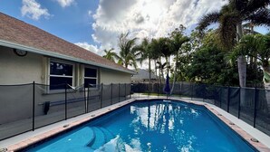 A rectangular swimming pool with a tiled edge, surrounded by a fence and palm trees. - Heated pool, pool table, heart of Wellington! (Wellington)
