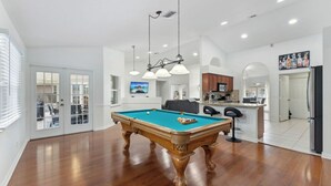 A spacious living room with a pool table, a kitchen area, and a dining space. - Heated pool, pool table, heart of Wellington! (Wellington)