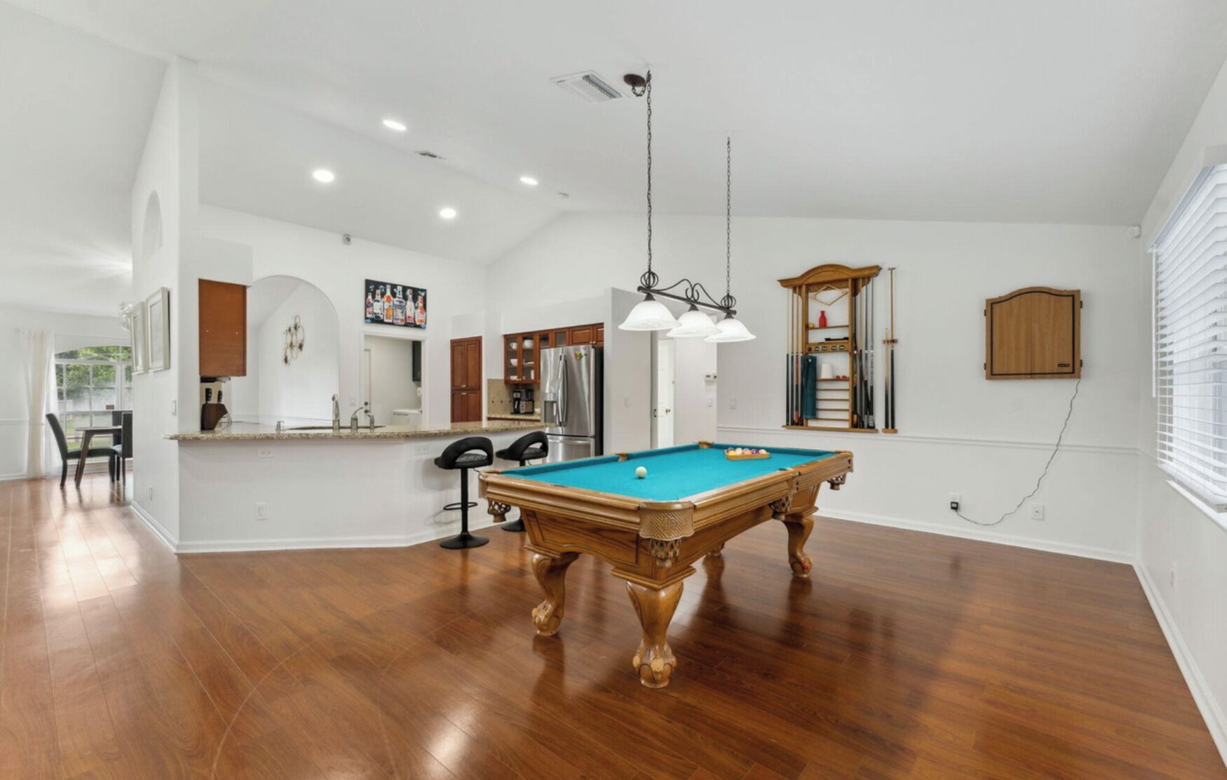 A spacious living area with a pool table, wooden flooring, and a kitchen area with modern appliances.