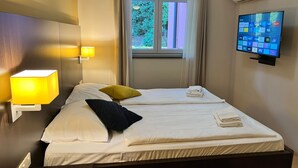 A hotel room with two beds, a TV, an air conditioner, and a window with curtains. - Marina Portorož Family Friendly Apartment 1 (Piran)