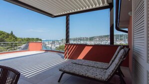 Un balcón con vista a un puerto deportivo, una silla acolchada y una mesa.