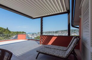 Un balcón con vista a un puerto deportivo, una silla acolchada y una mesa.