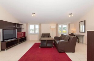 A modern living room with a flat-screen TV, a sofa, a coffee table, and a desk with a lamp.