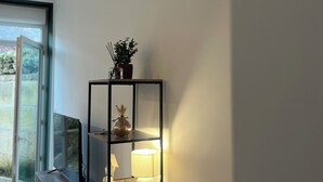 A modern interior with a wooden desk, a black metal shelf with decorative items, and a lit lamp.