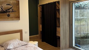 A bedroom with a large bed, a wooden headboard, a nightstand, a window with a view of the outdoors, and a door leading to a bathroom.