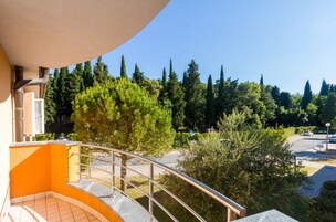A balcony with a metal railing overlooking a parking area and a row of trees.