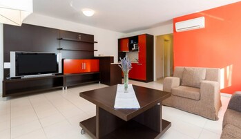 Una sala de estar moderna con un televisor de pantalla plana, armarios de madera oscura, una pared de acento roja y un sofá color beige.