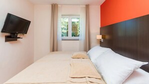 Hotelkamer met een bed, een aan de muur bevestigde televisie, een raam met gordijnen en uitzicht op groen.