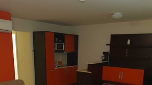 A hotel room with a bed, a sofa, a small table, a kitchenette, and a wardrobe.
